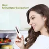 A woman is holding a small white and gold deodorizer in front of an open refrigerator. Náhľad obrázku produktu