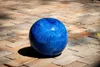 A blue ceramic garden ball rests on a brick patio. Produktbild-Vorschau
