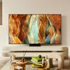A modern living room with a large TV displaying a colorful abstract image, placed on a minimalist stand. A coffee table in front of the TV holds decorative items and books. Voir les images du produit