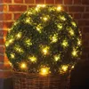 A spherical topiary decorated with warm white LED lights sits in a wicker basket against a brick wall. Produktbild-Vorschau
