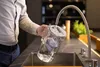 A person is filling a glass water filter pitcher from a faucet in a modern kitchen. Produktbild-Vorschau