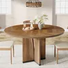 A round wooden dining table with a vase of flowers and a tray of snacks on it, set in a dining room with chairs and a chandelier. Voir les images du produit