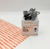 A Stihl carburetor is placed on its original packaging box, with a white background and a sheet of orange Stihl branded paper to the left. Produktbild-Vorschau