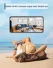 A person is lying on a beach, holding a smartphone that displays a virtual tour of a living room. Produktbild-Vorschau