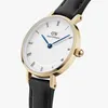 A close-up, angled view of a Daniel Wellington watch with a white face, gold casing, and black leather strap. Produktbild-Vorschau