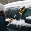 A person is using a snow brush to clear snow from a car window. Produktbild-Vorschau