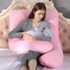 A woman is holding a baby while sitting on a bed with a large pink U-shaped pillow. Produktbild-Vorschau