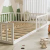 A child's bed frame with wooden slats and white railings, set in a room with a mountain-themed mural on the wall and a fluffy toy in the background. Anteprima dell’immagine prodotto