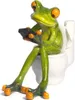 A decorative figurine of a green frog sitting on a toilet and holding a remote control. Produktbild-Vorschau