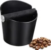 A black coffee knock box with a metal and rubber bar, placed next to a pile of coffee beans on a white background. Produktbild-Vorschau