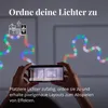 A person is holding a smartphone, using an app to control a string of multicolor LED lights arranged in a wavy pattern on a wall. Produktbild-Vorschau