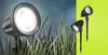 Two garden spotlights are shown, one larger in the foreground amongst grass, and two smaller ones in the background against a green backdrop. Náhled obrázku produktu