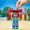 A toy Optimus Prime robot is shown in a backyard setting with a small human figure being held above it. Podgląd zdjęcia produktu