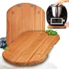 Two wooden cutting boards are shown, one in the foreground and one behind it. A black kitchen appliance with a silver bowl is on the back cutting board, and a hand is reaching towards it. Blueberries and a sprig of basil are also visible. Produktbild-Vorschau