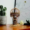 A wooden model hot air balloon sits on a wooden surface, with a potted cactus and a white rose in the background. Anteprima dell’immagine prodotto