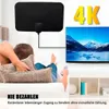 Schwarze Flachbild-TV-Antenne an einer weißen Wand über einem Fernseher montiert, mit einer Person, die auf einem Sofa fernsieht Productafbeelding-voorbeeld
