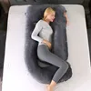 A woman is sleeping on a bed, using a large U-shaped pillow. Produktbild-Vorschau