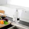 A white electric hot water tap is shown in a kitchen setting next to a sink, with some vegetables on a cutting board in the foreground. Náhled obrázku produktu
