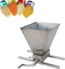 A stainless steel manual grain mill with a hopper and a crank handle, shown with four small containers of different grains or spices. Podgląd zdjęcia produktu