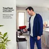 A man is emptying a red and black cordless vacuum cleaner into a silver dustbin in a kitchen. Voir les images du produit