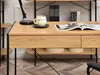 A close-up view of a wooden desk with black metal legs, showing a drawer, a shelf with round containers, and a magazine on top. Náhled obrázku produktu