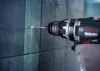 A person wearing a white glove is using a Bosch drill to drill a hole in a tiled wall. Podgląd zdjęcia produktu