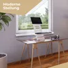 A laptop stand and keyboard are set up on a glass-topped desk in front of a window, with a plant in the foreground. Produktbild-Vorschau