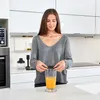 A woman in a kitchen is holding a lid over a glass of orange juice. Podgląd zdjęcia produktu