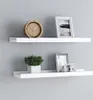 Two white floating shelves mounted on a light gray wall. The top shelf holds a wooden clock and a silver framed picture. The bottom shelf holds a small potted plant and two silver framed pictures. Anteprima dell’immagine prodotto