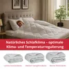 A woman sleeping under a white duvet on a bed, with three folded duvets shown below. Produktbild-Vorschau