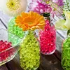 Close-up of several glass vases filled with colorful water beads and flowers, arranged on a wooden surface. Produktbild-Vorschau