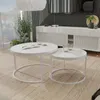 A modern living room scene with two white nesting coffee tables in the foreground, a white sideboard in the background, and large windows with greenery visible. Voir les images du produit