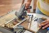A person is using a DREMEL® Blueprint Mobile Sägestation to cut a piece of wood flooring. Produktbild-Vorschau