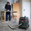 A person is using a Starmix industrial vacuum cleaner while working on a wooden board. Produktbild-Vorschau