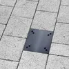 A dark gray metal base plate with screw holes is embedded in a paved surface made of light gray concrete blocks. Náhľad obrázku produktu