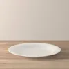 A white plate is centered on a wooden surface against a plain, light-colored wall. Náhľad obrázku produktu