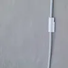 A close-up shot of a white cable clip attached to a gray wall, holding a white cable. Produktbild-Vorschau