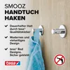 Two tesa SMOOZ towel hooks mounted on a wooden wall, one with a blue towel hanging from it. Text describes product features. Náhled obrázku produktu