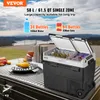 A portable car refrigerator is shown open and filled with drinks, placed on a table outdoors with a scenic view of a lake and mountains in the background. Náhled obrázku produktu