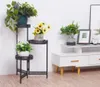 A plant stand with three tiers holding various potted plants, placed next to a white media console. Náhľad obrázku produktu