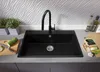 A black kitchen sink with a black faucet, set against a textured white backsplash. A cutting board with a zucchini and knife is to the left, and a paper bag with groceries is to the right. Produktbild-Vorschau
