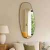 A modern living room with a couch, lamp, and a large, organically shaped mirror on the wall. Produktbild-Vorschau
