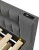 Close-up view of a gray upholstered bed frame, showing the headboard and the wooden slats of the mattress support. A black USB charging port is visible on the side of the headboard. Podgląd zdjęcia produktu