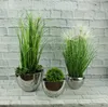 Three silver ceramic planters with artificial plants are displayed against a white brick wall. Podgląd zdjęcia produktu