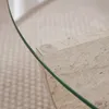 A close-up view of a round glass-top coffee table with a travertine base, resting on a carpeted floor. Anteprima dell’immagine prodotto