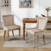 Two beige upholstered dining chairs are placed around a wooden dining table in a well-lit room. Podgląd zdjęcia produktu