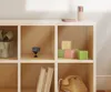 A shelf unit with various items, including a gift box, a small microphone, building blocks, books, and a rotary phone. Produktbild-Vorschau