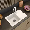 A modern kitchen sink with a faucet running water into it, set on a dark countertop with wooden cabinets and a knife block in the background. Náhľad obrázku produktu