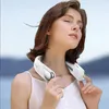 A woman wearing a neck fan outdoors with a blurred background of water and sky. Produktbild-Vorschau