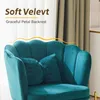A close-up of a teal velvet armchair with a scalloped backrest and two decorative pillows. Beige curtains are visible in the background. Anteprima dell’immagine prodotto